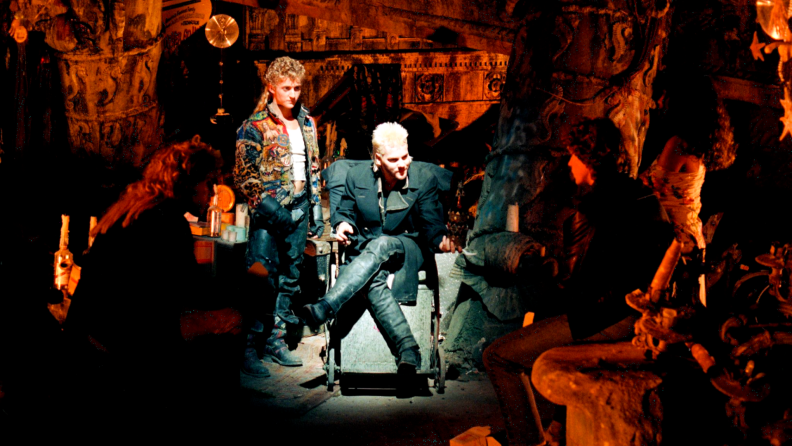 A young Kiefer Sutherland sits on a makeshift throne in a vampire hideout. To his left is actor Alex Winter; on his right, Lost Boys star Jason Patric.