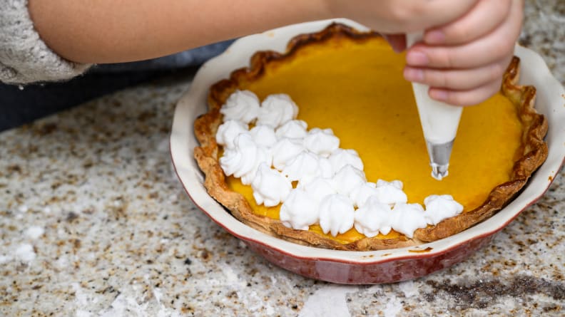 A person piping merengue onto a pumpkin pie.