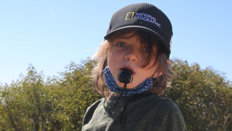 A young boy mischievously looks in the camera as he blows a camping whistle.