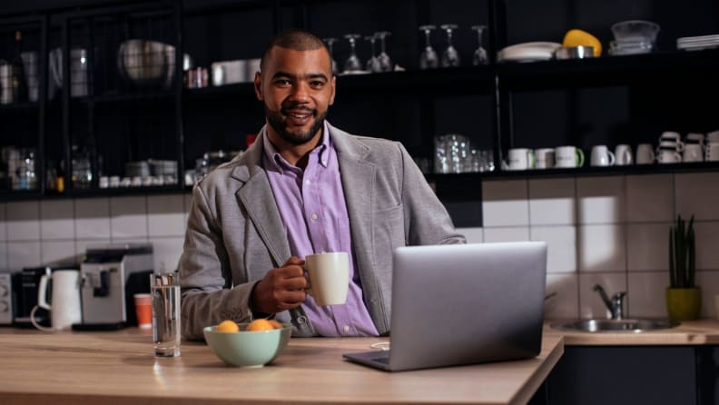 Man holding mug and dressed in professional work attire in front of laptop.