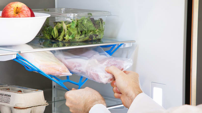 A hand pulls down a special net inside a refrigerator meant to hold deli meats.