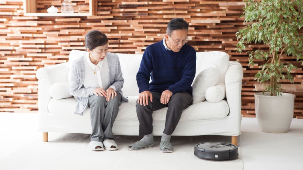 Older couple sitting on couch together watching robot vacuum clean.