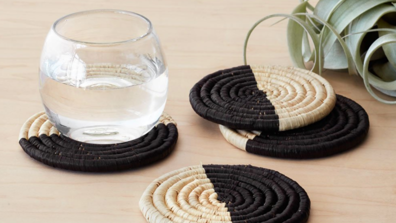 Three natural tan and black color block coasters with a glass of water on a wooden counter