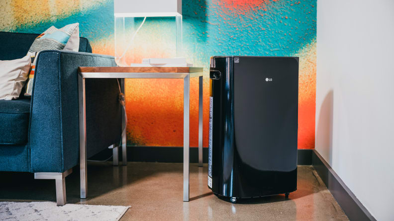 A black LG Puricare dehumidifier sits next to a table and couch with a colorful wall in the background.