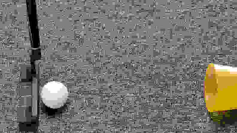 A golf putter and a golf ball on a carpet next to a plastic cup