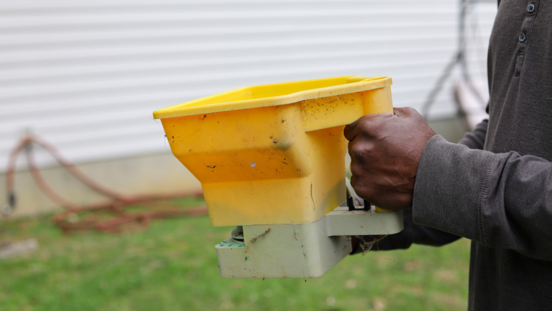 Person using hand-held seed spreader in yard