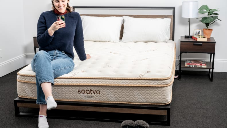 a person sits on the edge of the Saatva classic mattress