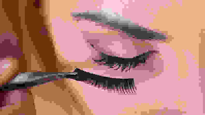 A woman applying a pair of fake eyelashes.