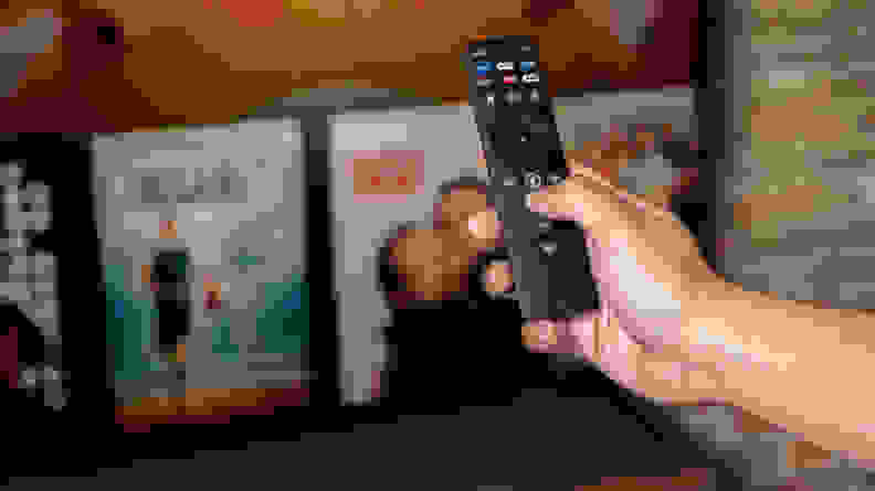 A hand holding a remote in front of the TV.