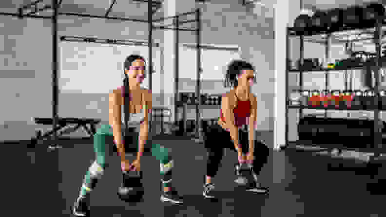 Two women squatting with kettlebells at the gym.