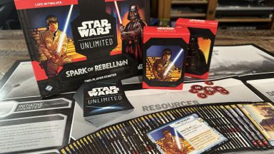 The Star Wars: Unlimited card game, with cards fanned out in front of a deck of cards, cardboard tokens, two deck boxes with images of Luke Skywalker and Darth Vader, the game box with the same images, and a foldable playmat.