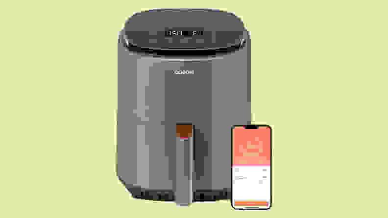 Cosori Lite four-quart air fryer with smartphone next to it in front of green background
