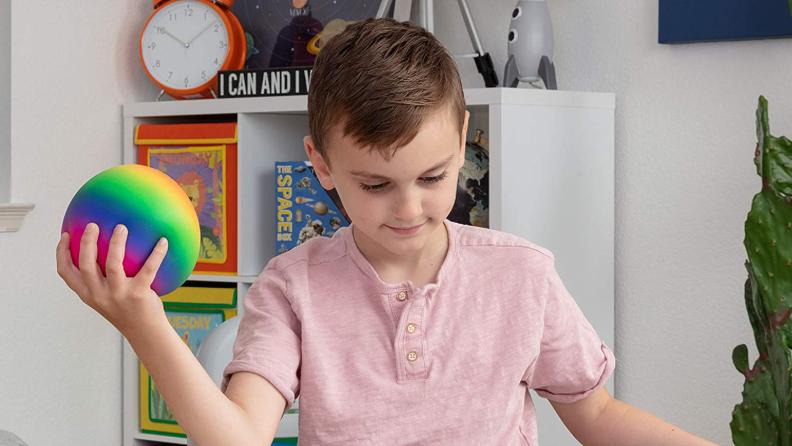 A child squeezes a colorful ball with one hand while sitting down.