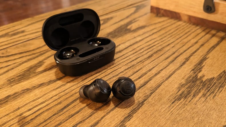 The JBL Quantum TWS Air earbuds on a wood table.