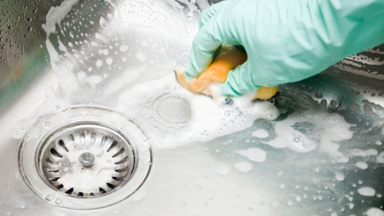 A person wipes a stainless steel sink with soap.