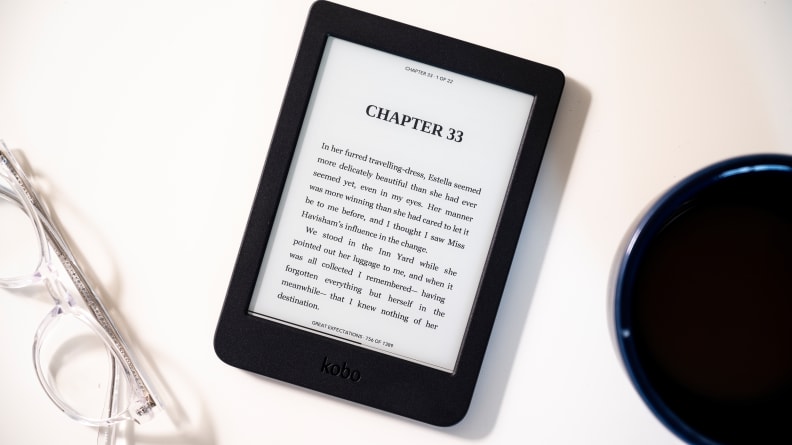 Black e-reader on white surface next to reading glasses
