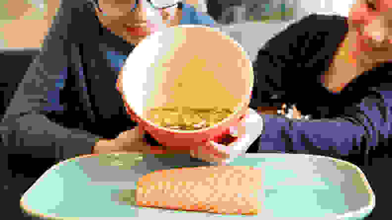 A boy and a girl pouring marinade on a piece of salmon