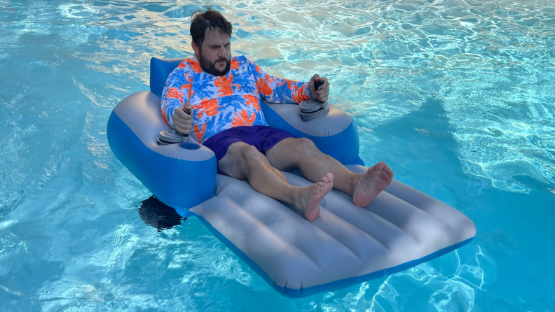 Person reclining on top of the Sharper Image Motorized Pool Lounger in pool water outdoors.