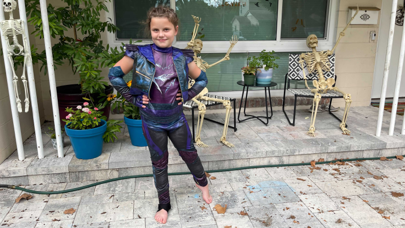 A girl dressed up as Mal from Descendants 3 standing on a porch decorated with skeletons