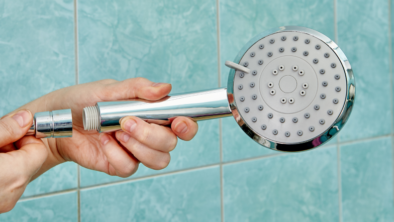 A person disconnects a shower head.