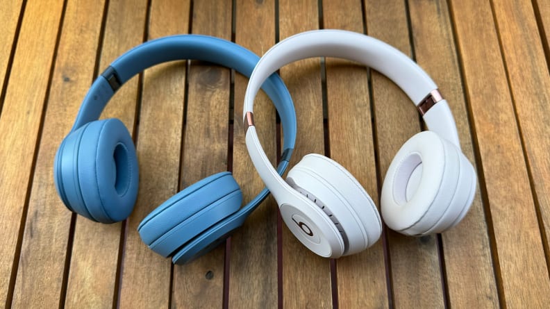 Two Beats Solo 4 headphones, one in Slate Blue and one in Cloud Pink, resting on a wooden table.