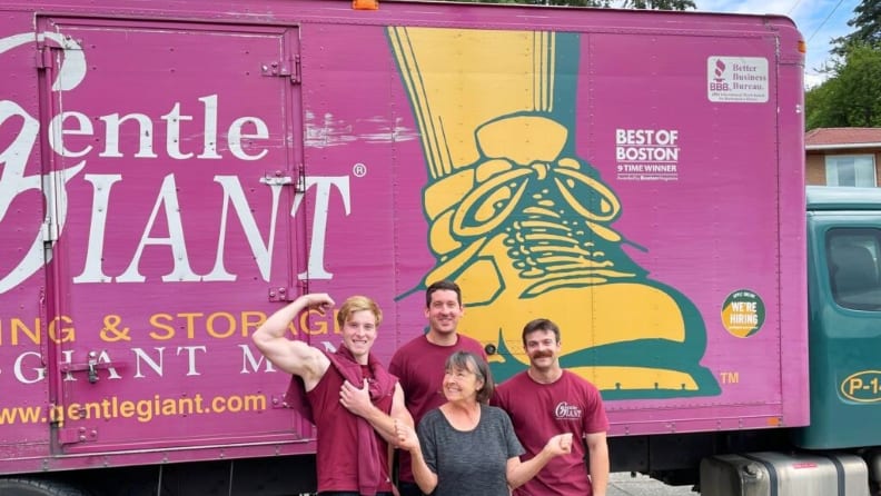 An image of four members of a moving company with their company truck behind them