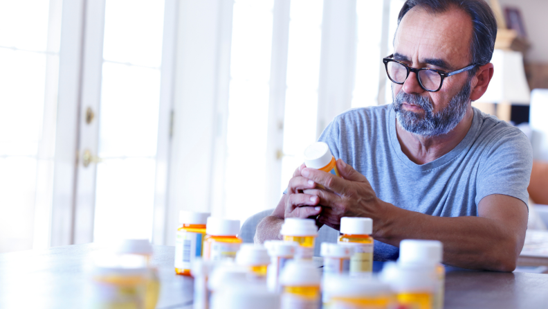 Person sitting at table surveying medication bottles.