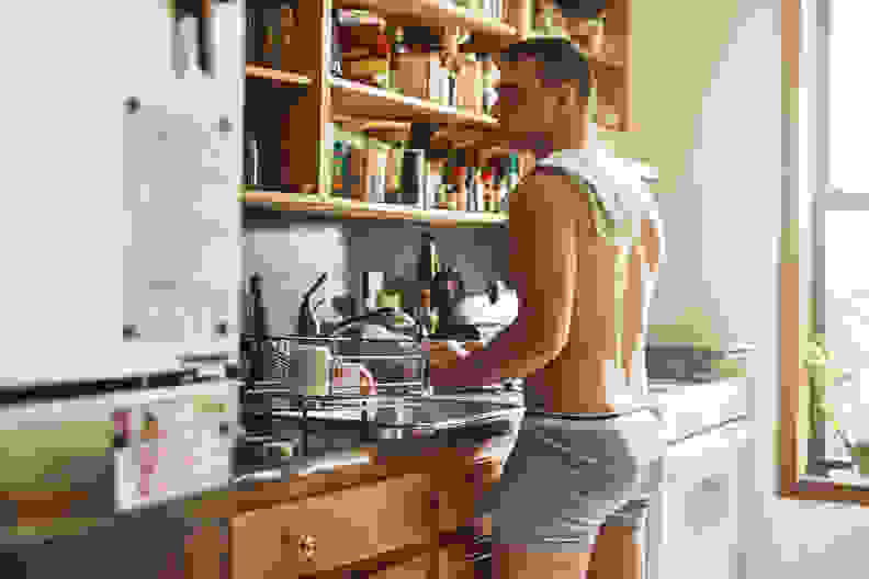 A man dressed in boxer briefs washes dishes.