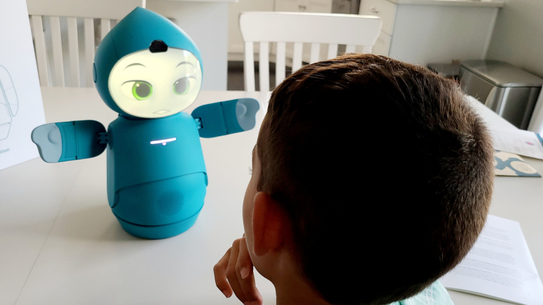 Child sitting in front of Moxie robot while sitting at kitchen table.