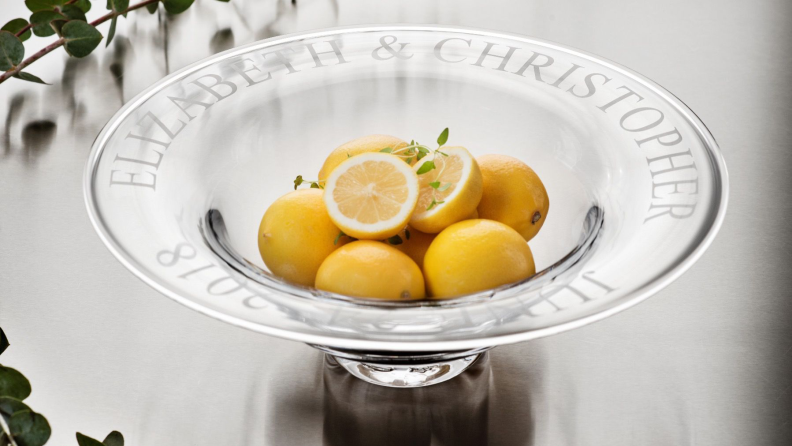 An engraved glass bowl holding some fresh lemons.