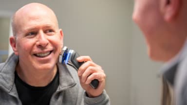 A man looks in his bathroom mirror as he shaves his face.