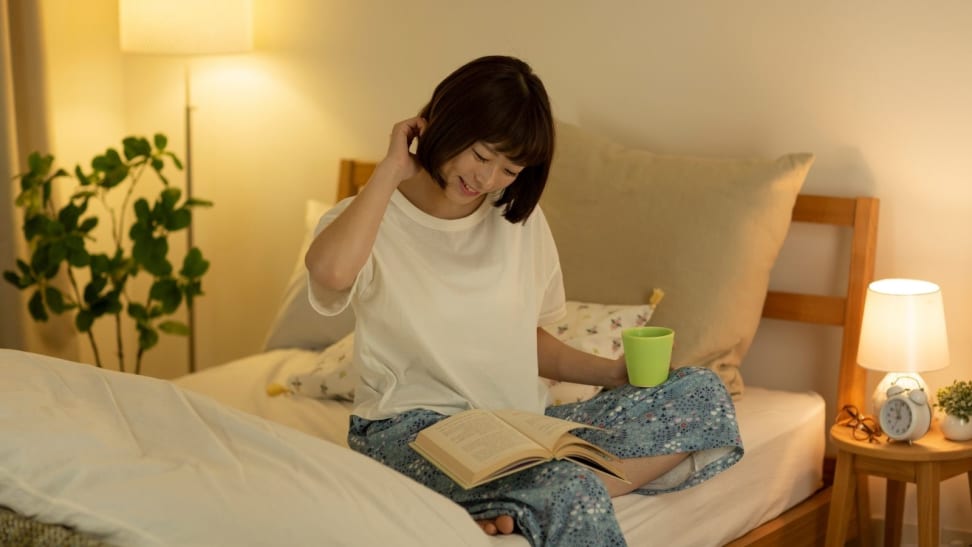 Woman on bed with book and mug.