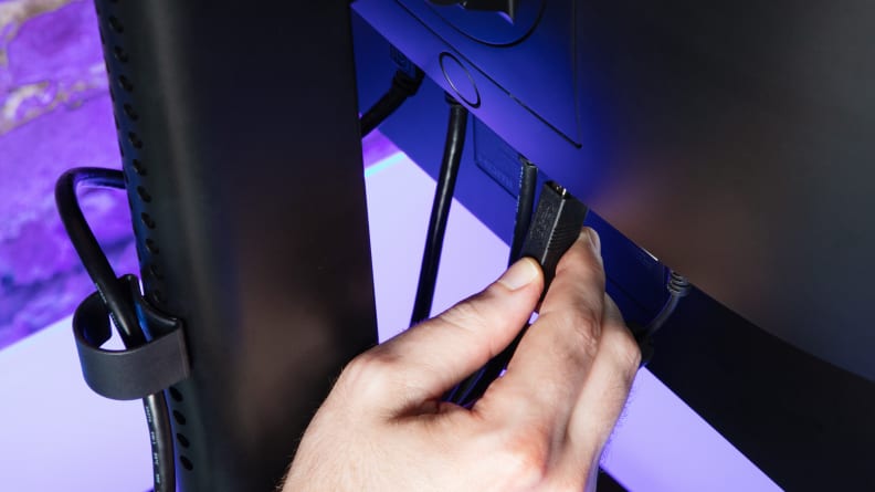 A hand plugs a USB cable into a USB port on the back of the NZXT Canvas 27Q.