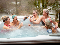 A group of friends drink champagne while sitting in a hot tub.