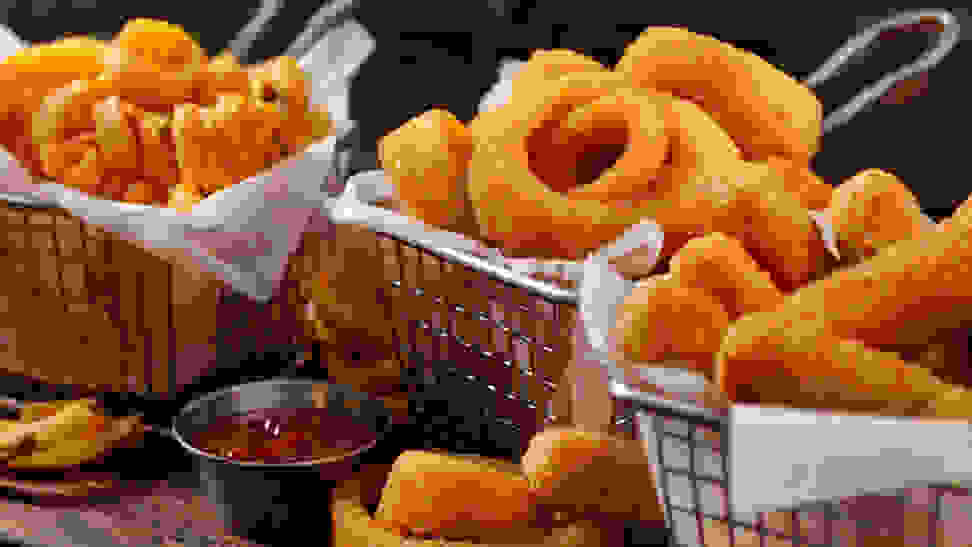 Fried onion rings and french fries are piled up in fry baskets.
