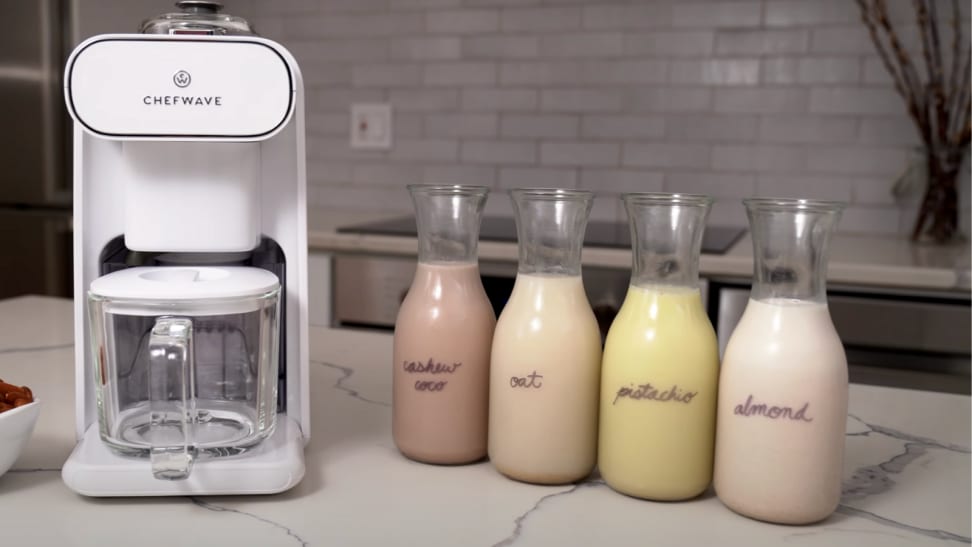 On a kitchen counter, there's a ChefWave Milkmade vegan milk maker with four bottles of nut milk next to it.