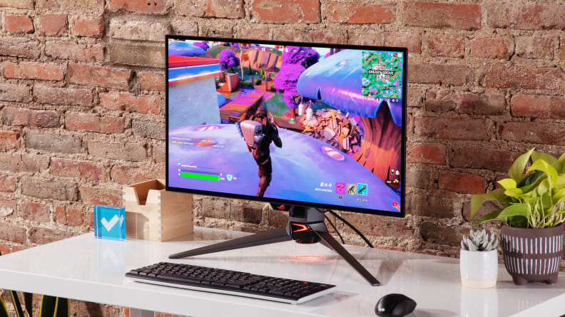Asus ROG Swift OLED PG27AQDM sitting on top of desk in front of brick wall.