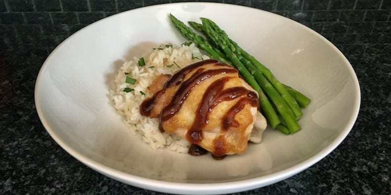 A white plate is filled with rice,  a perfectly cooked chicken breast, and asparagus spears.