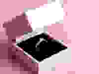 This is an engagement ring in a white box against a pink background.