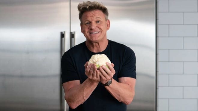 Chef Gordon Ramsay holds a clump of dough in a kitchen.