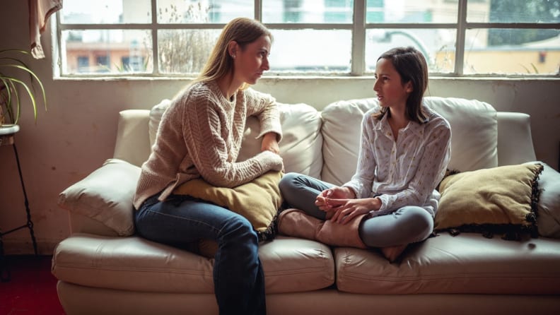 A mom and daughter talk seriously while sitting on a couch.