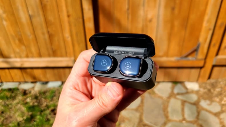 Master & Dynamic MW08 sit within their open case in front of a cedar gate.
