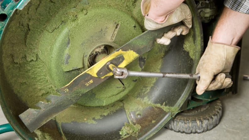 Person uses gloves and wrench to unscrew blade on lawn mower.