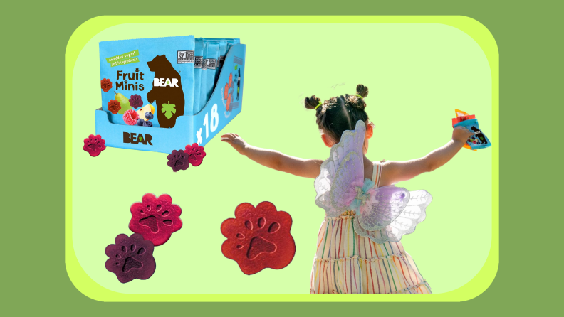 Several Bear Real Fruit Snacks packages lined up in cardboard display box next to small child with arms raised in the air while one hand holds two packages of fruit snacks.