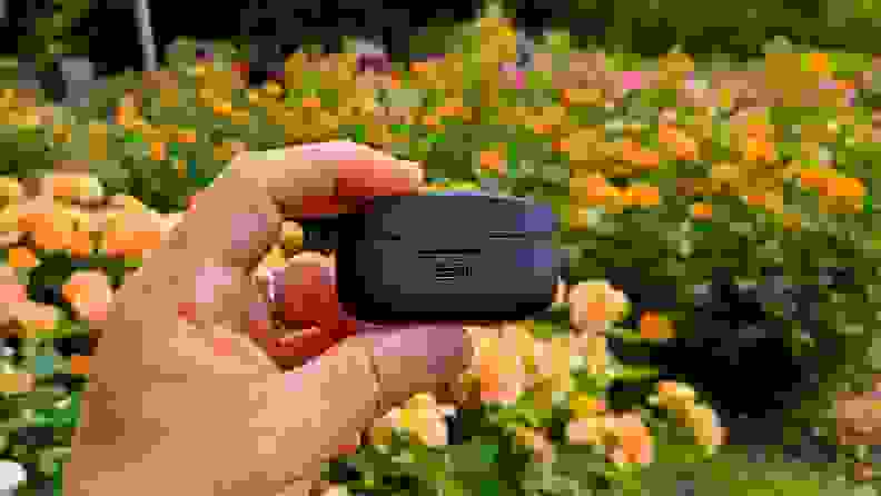 The all-black Sony WF-1000XM4 are shown within their case from the back to expose their USB-C port with a backdrop of yellow roses