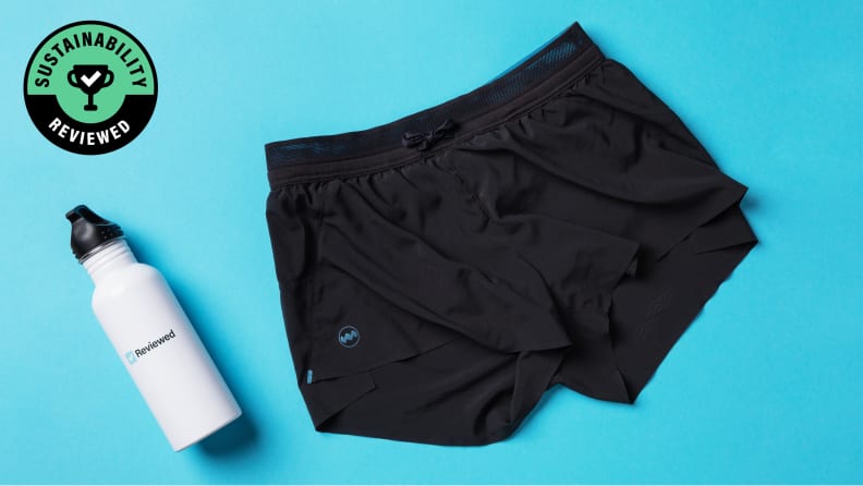 A white water bottle with the Reviewed logo lying down next to a pair of black shorts from Janji.