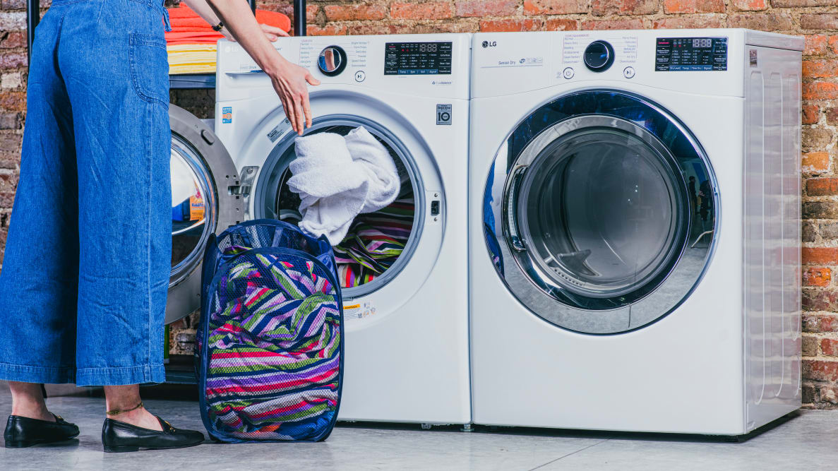 Woman loading a white towel into the white LG WM3700HWA front-loading washing machine, which is sitting next to a matching front-loading dryer.