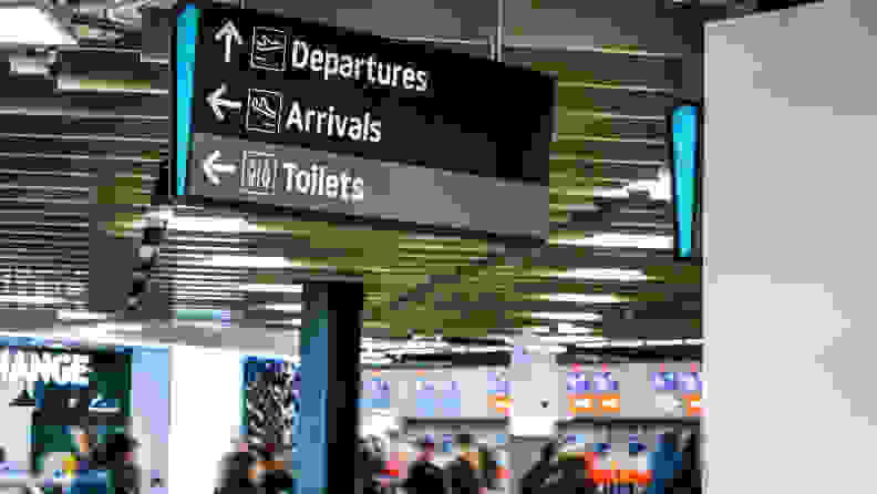 Blurred anonymous people walking under information table, under arrival, departure, and toilets sign at the airport.