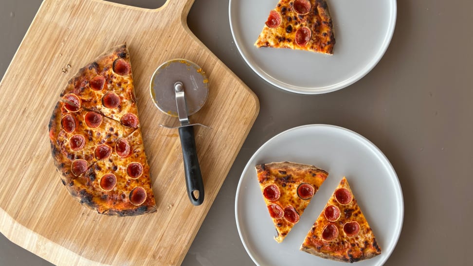A pepperoni pizza and pizza cutter on a board next to plates with slices.