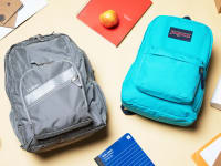 An L.L. Bean backpack and JanSport backpack laying on a table surrounded by school supplies and apples.